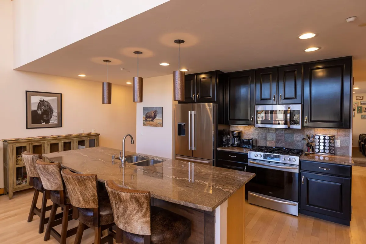 A spacious, open-plan kitchen featuring a central island with stools, surrounded by stainless steel appliances. The space is bright and inviting, with artwork adorning the walls, creating an atmosphere ideal for cooking, entertaining, and family gatherings.