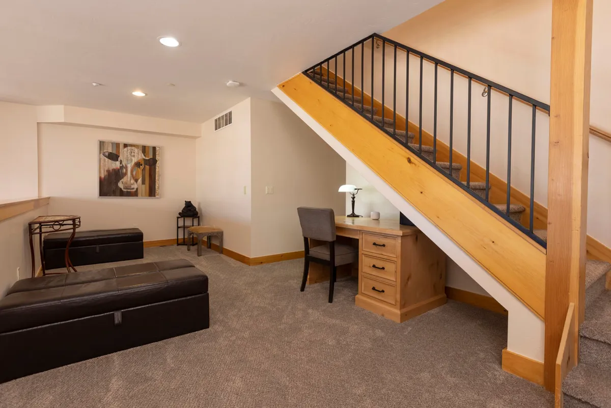 This interior image showcases a welcoming entryway featuring a staircase, a desk with a lamp, and a comfortable seating area. The space is practical for transitioning from the outdoors to the comfort of home, offering both storage and a resting spot.