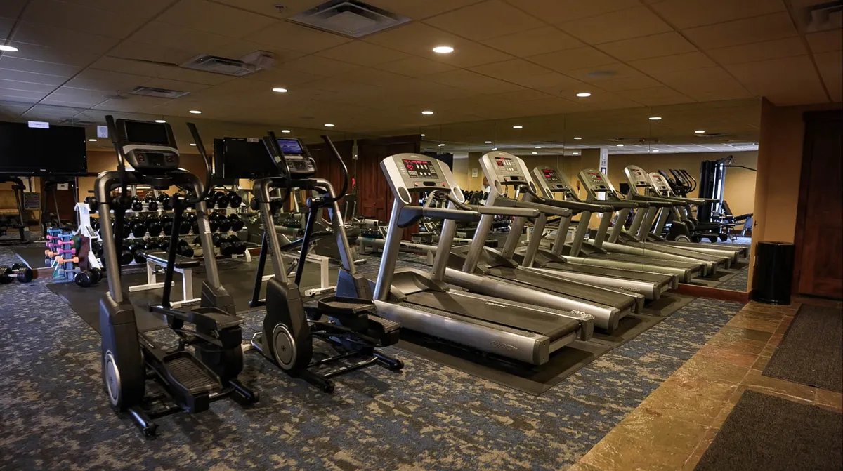 A well-equipped, mirrored fitness area with treadmills, ellipticals, dumbbells, and ample space, evoking a sense of readiness and preparation before hitting the slopes.