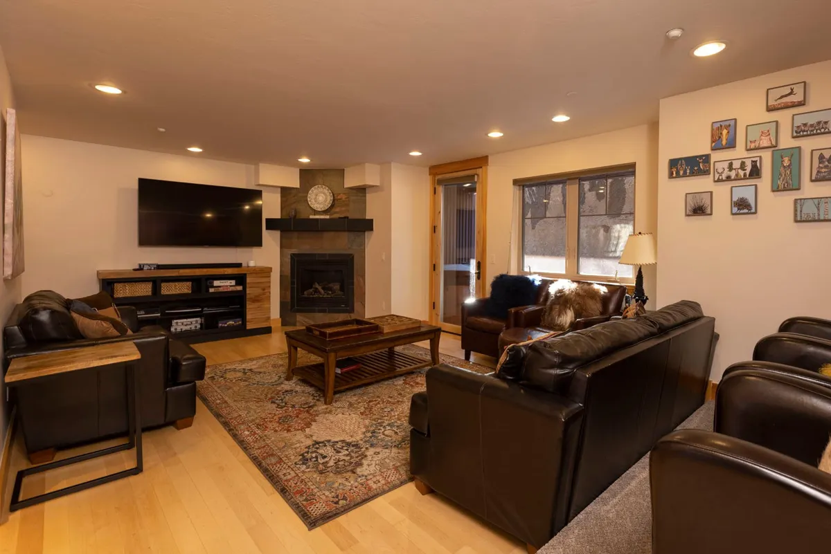 A spacious living room anchored by a stone fireplace, surrounded by a plush sofa set, a coffee table, and wall artwork. The design exudes comfort and invites gatherings for relaxation, socializing, watching TV, or enjoying a fireside chat.