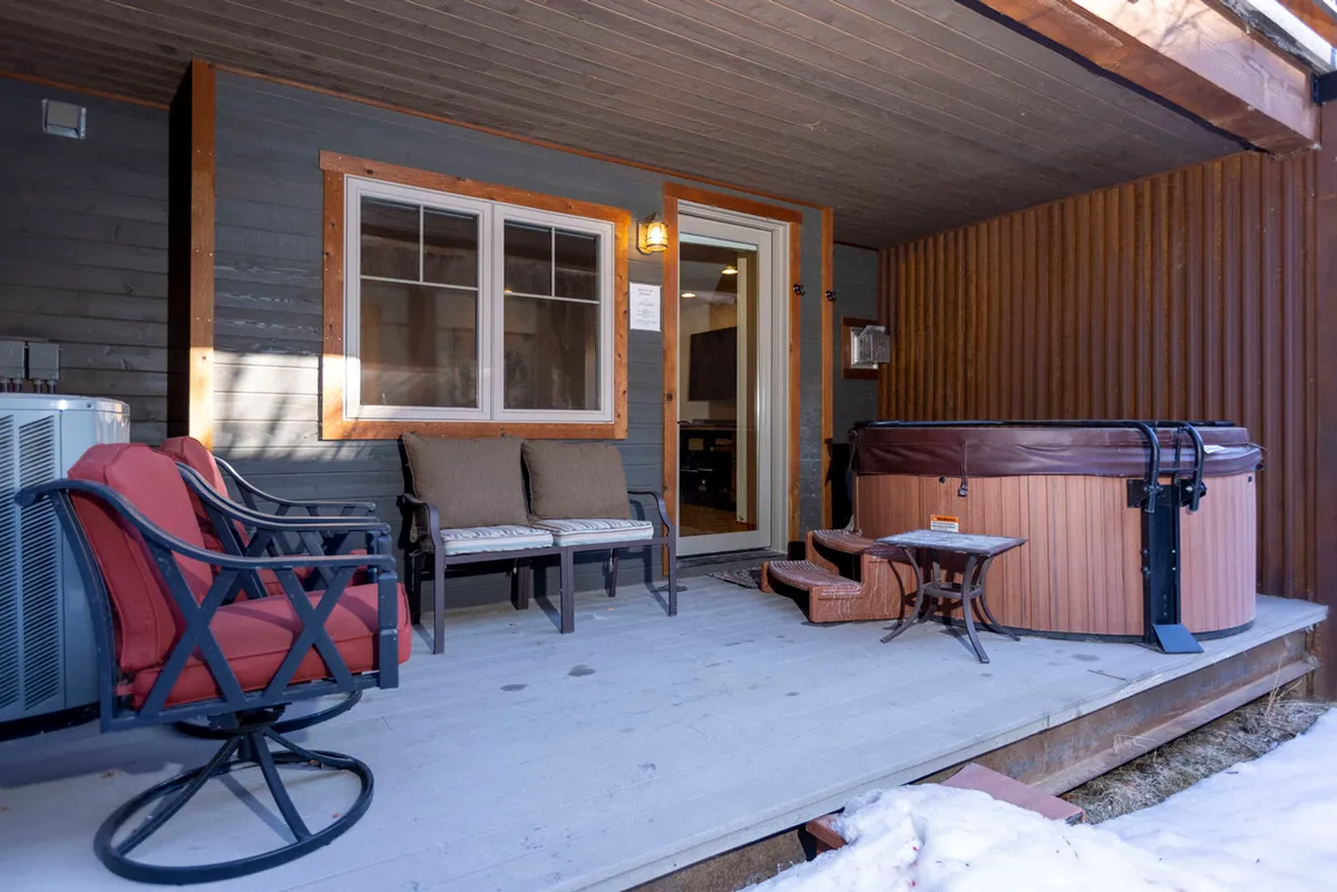 An exterior seating area with a hot tub and gathering space near the entrance, set against a backdrop of snow and mountain views. The setup is perfect for stepping out from the living area to enjoy fresh air and scenic vistas.