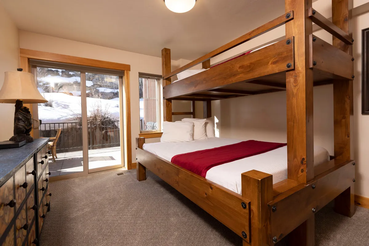A family-friendly bedroom with a bunk bed and dresser, complemented by a sliding glass door that opens to a view. The space is practical yet cozy, appealing to children or teens and exemplifying flexible sleeping arrangements.