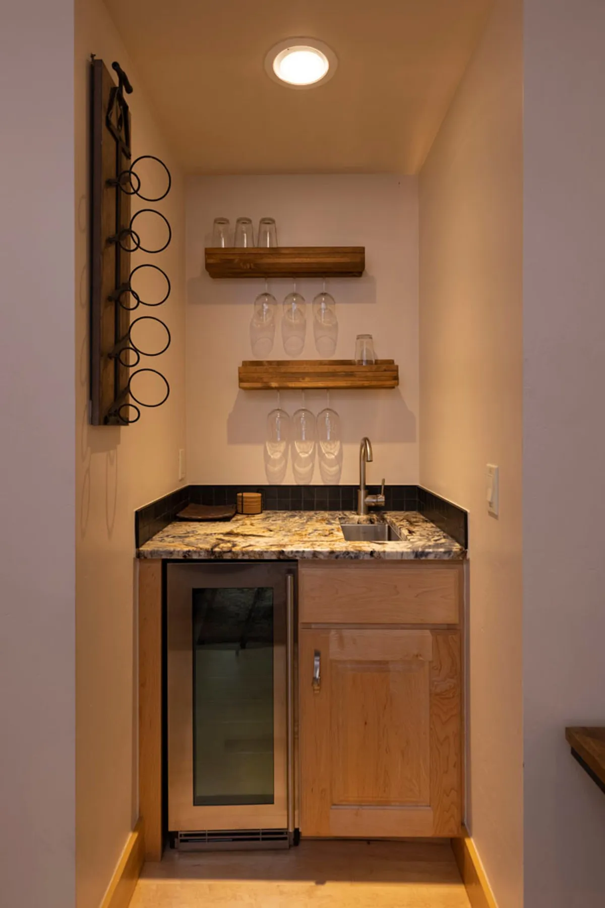 A granite countertop adorned with glassware, a built-in wine rack, and a large refrigerator create a cozy yet sophisticated setting. The scene suggests a space ideal for entertaining guests, preparing drinks, and sharing intimate conversations.